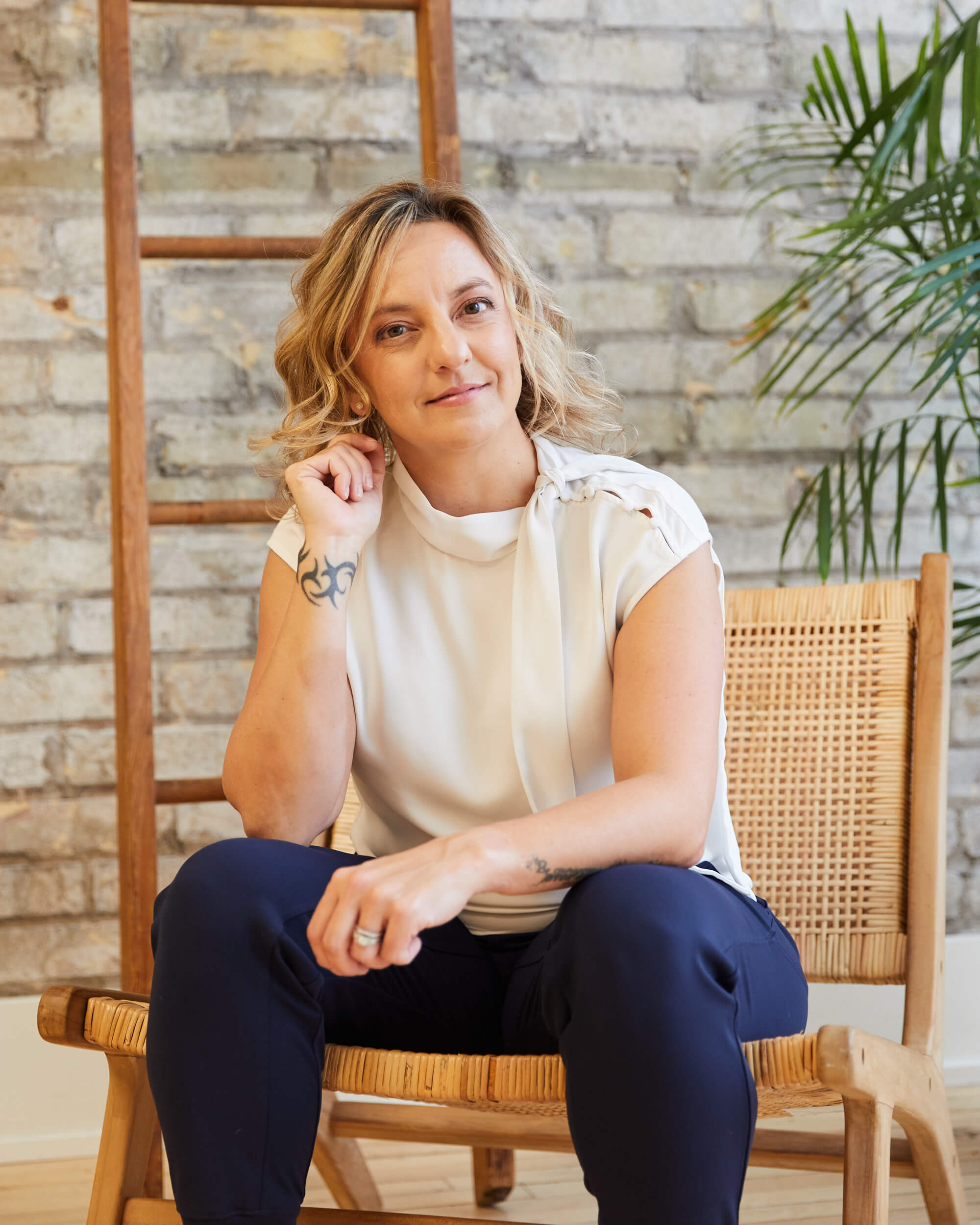 Michelle Martin sits in a rattan chair inside a brick office building. There is a palm tree beside her.