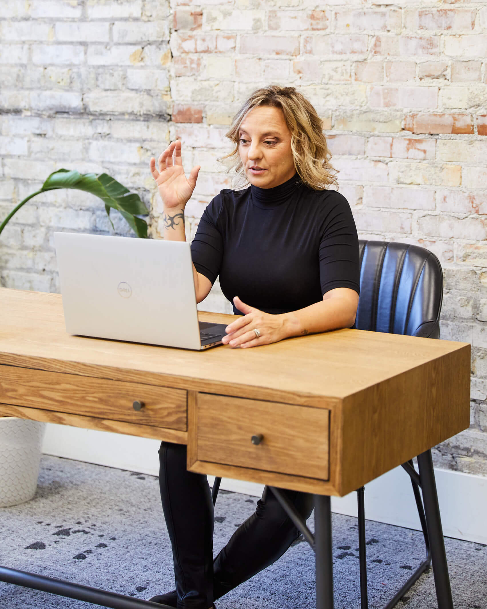 Michelle sits behind a wooden desk and has her laptop open. She is facing the computer and speaking to someone virtually.